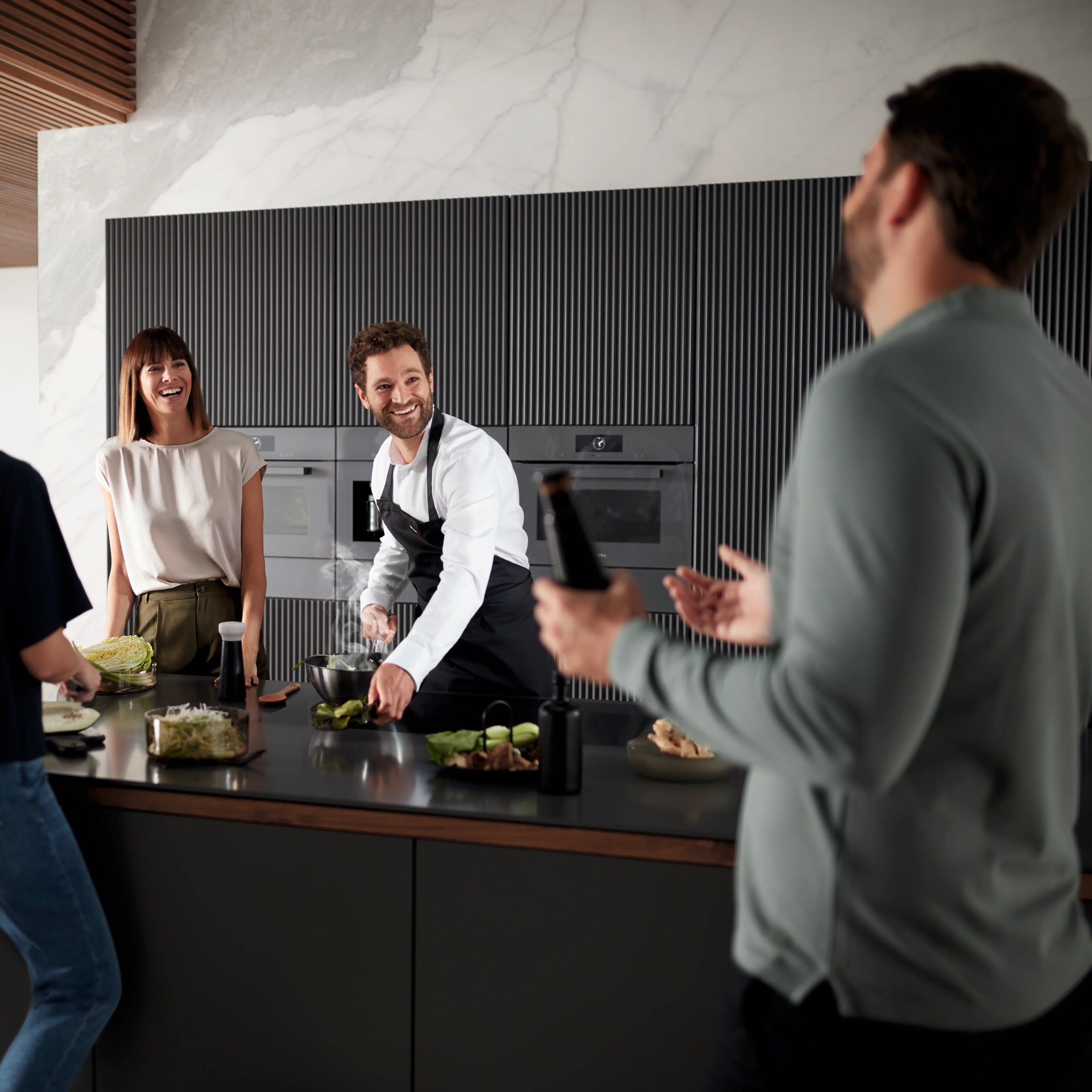 Chef preparando wok en cocina Miele con hornos integrados amigos alrededor de isla