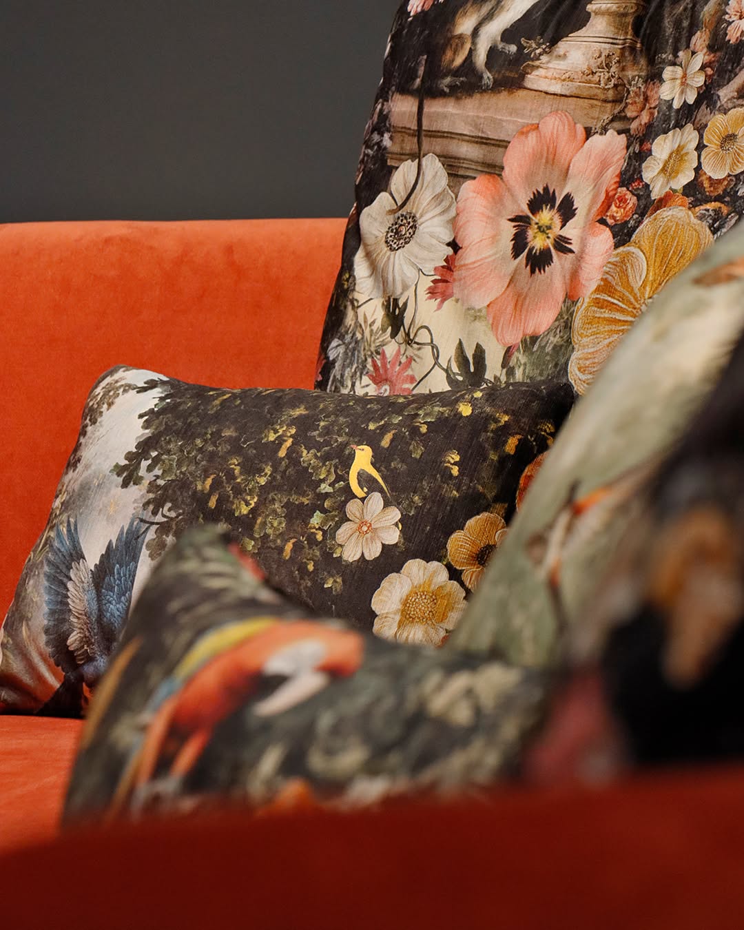 Detail of Fama cushions with floral and bird prints on a sofa upholstered in orange velvet
